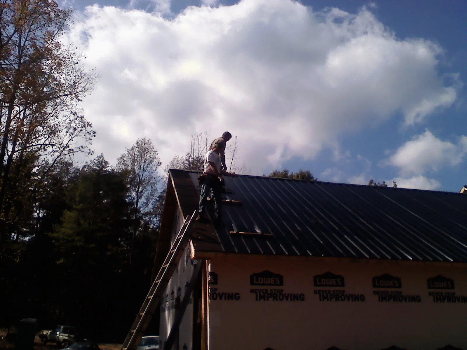 Roofer fastening dark metal panels high against a cloudy sky, from a Roof Inspection job in El Granada